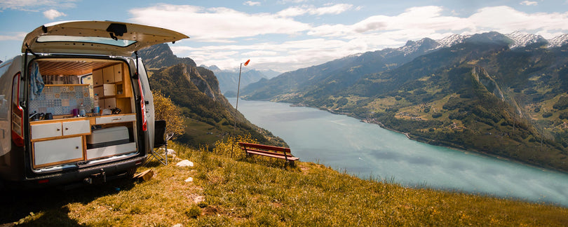 Van conversion with kitchen setup on a mountain top overlooking a lake and mountains.